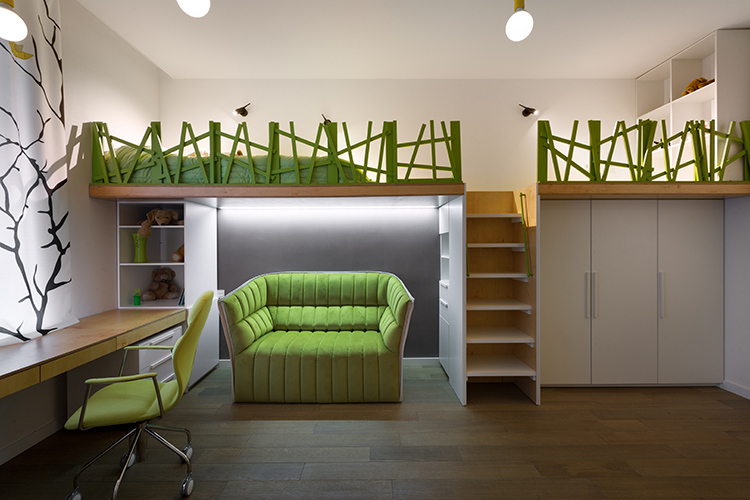 SOLUTIONS: For the teenage daughter, the designer created a stylish, multifunctional room with two beds, a work desk, and a comfortable, bright sofa. She went with a natural green, white and oak palette. BELOW: In the second room, intended for a boy, two beds are hidden under a wooden podium. A work desk placed near the window clears more space for fun and study. The white walls are decorated by blue and red wall art – a convenient way to dress up a child’s room — delivering simplicity with a punch of character.
