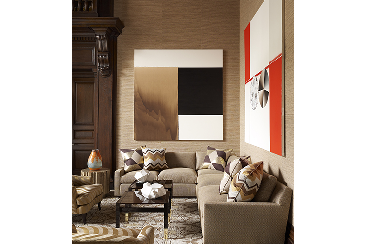 Calm, neutral tones set the scene in the living room and serve as a backdrop for modern art. Black, brown and white oil painting by Callum Innes. Orange and white oil painting by Garth Weiser. Wood and polished brass cocktail tables from Lorin Marsh. Braided hemp wallcovering by Maya Romanoff. Custom area rug from Stark for Bhutan Collection. Sofa upholstered by Jonas Upholstery with Donghia fabric. Vintage upholstered chairs