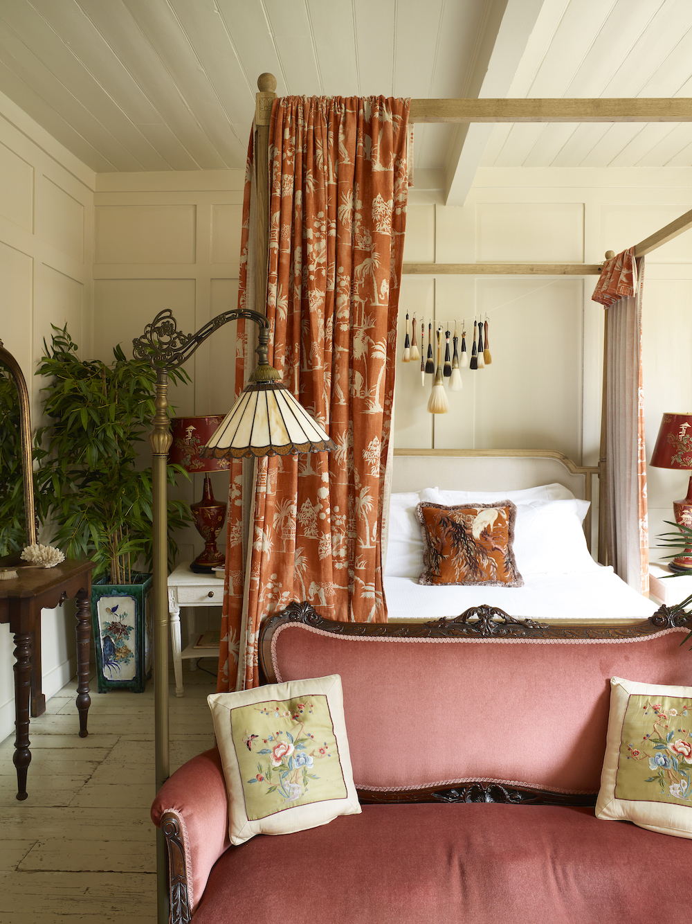 Bedroom in London's East End with curtained four-poster bed and a rosy-hued velvet sofa set at its foot.