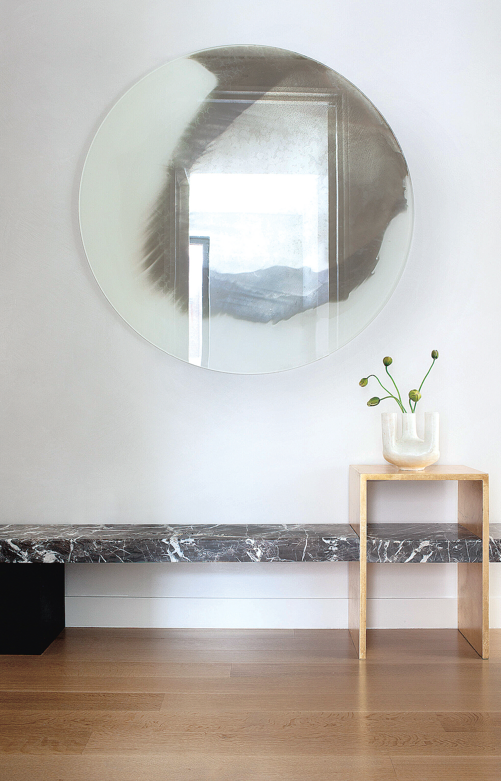 entry foyer of a Greenwich Village Pied-À-Terre featuring a long black marble bench and circular liquid silver-treated wall mirror